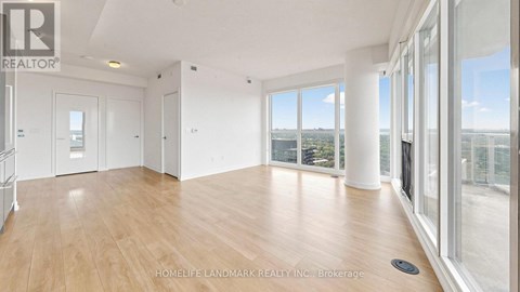 A spacious room with wooden flooring and large windows overlooking a cityscape.
