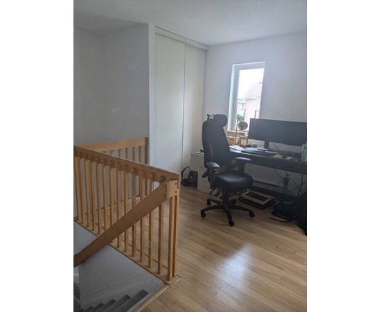 A room with a wooden staircase and a black office chair.