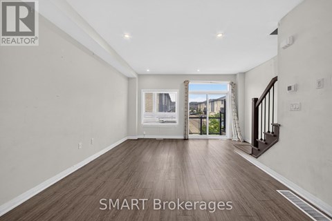 A spacious room with wooden flooring and a view of a cityscape through the window.