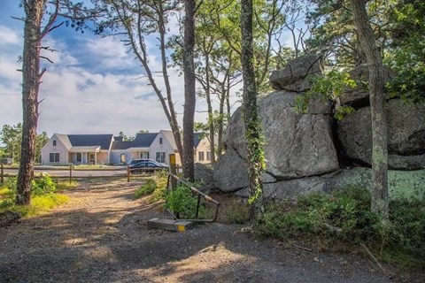 A large rock formation is in the foreground of a house surrounded by trees.