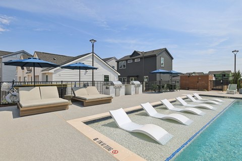 A pool with lounge chairs and umbrellas in front of a building.