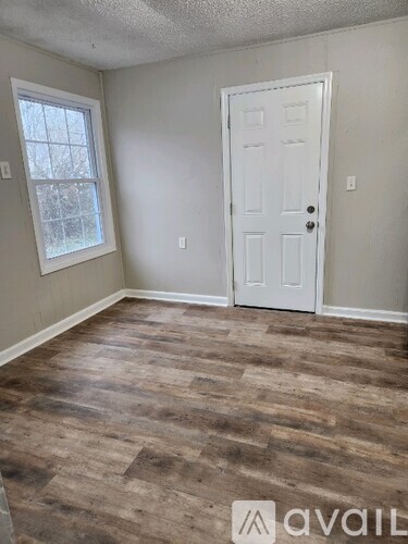 A room with a white door and a window with a view of trees.