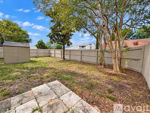 A backyard with a fence, trees, and a stone bench.