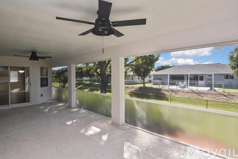 A room with a ceiling fan and a view of a house and trees outside.