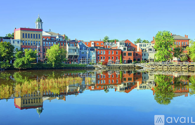 A serene lake reflects the colorful buildings and clear blue sky in the background.