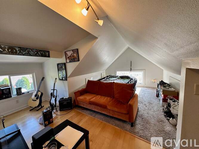 A living room with a brown couch and a guitar on the wall.