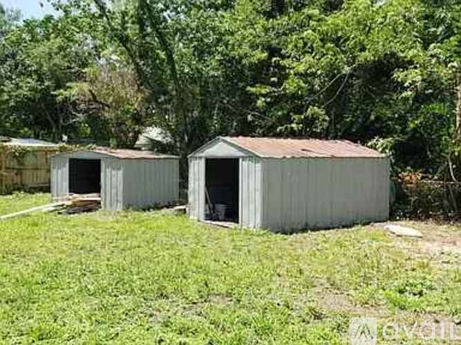 Two grey metal sheds are situated in a grassy area.
