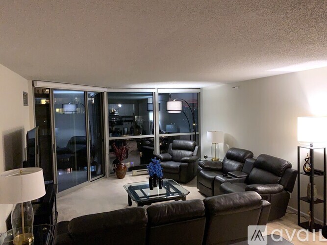 A living room with a brown leather couch and a glass table with a vase of flowers on it.