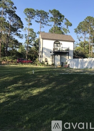 A white house with a balcony is surrounded by greenery.