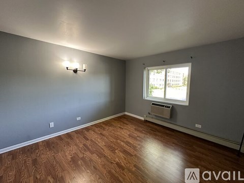 A room with wooden flooring and a window with an air conditioner underneath it.