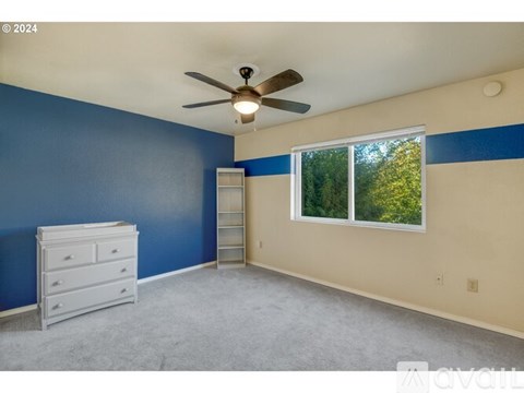 A room with a ceiling fan and a window showing trees outside.