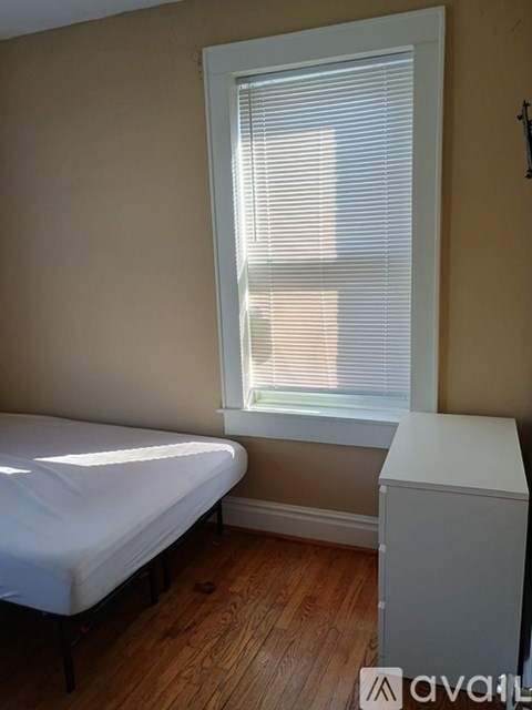A bedroom with a bed, a window with blinds, and a white dresser.