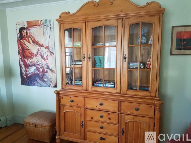A wooden cabinet with glass doors stands in a room with a painting on the wall.