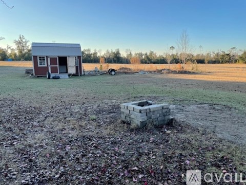 A small red and white building sits in a field with a trailer and a concrete block nearby.