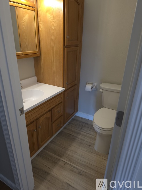A bathroom with a toilet, sink, and wooden cabinets.