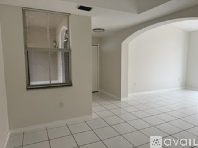 A spacious room with white tiled flooring and a window with a white frame.