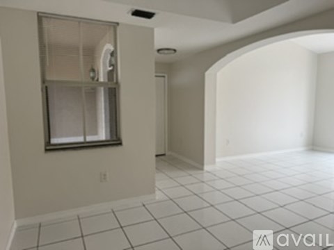 A spacious room with white tiled flooring and a window with a white frame.