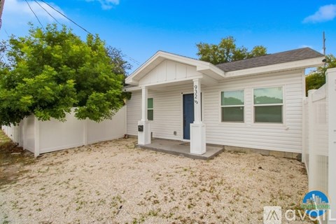 A small white house with a gravel driveway and a tree in front.