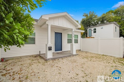A small white house with a porch and a fence in the yard.