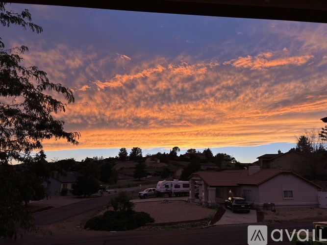 A sunset view from a window with a house and trees in the foreground.