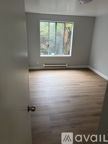A room with wooden flooring and a window with a view of trees.