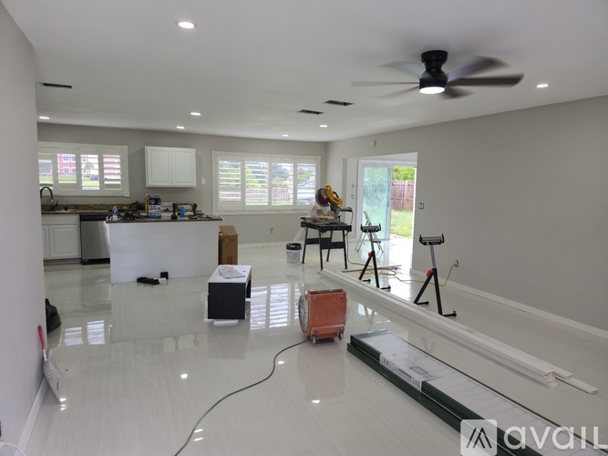 A room with a ceiling fan and a kitchen area in the background.