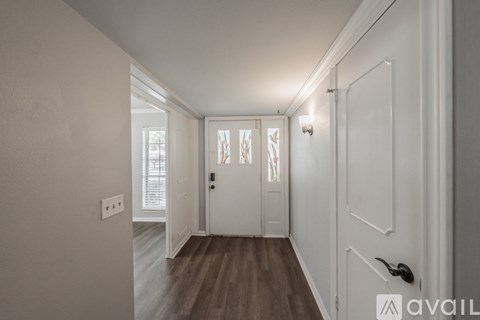 A hallway with a wooden floor and white walls leading to a door.