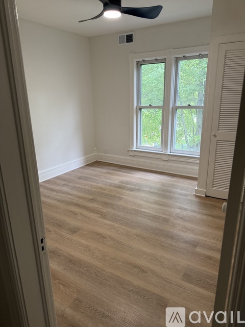 A room with a ceiling fan and a window with a view of trees.