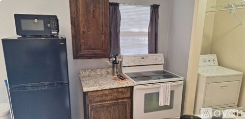 A black refrigerator sits next to a white stove in a small kitchen.