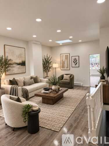 A living room with a white couch, a brown coffee table, and a white chair with a green plant on it.