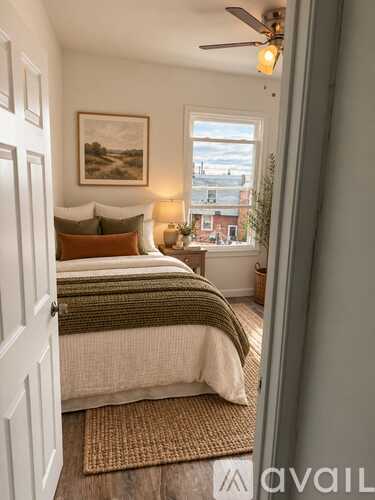 A bedroom with a bed, pillows, a blanket, a ceiling fan, and a window overlooking a cityscape.