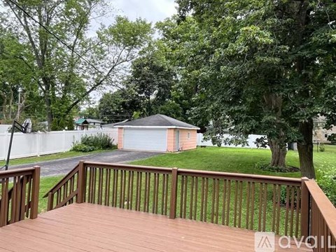 A deck with a railing overlooks a yard with a shed and trees.