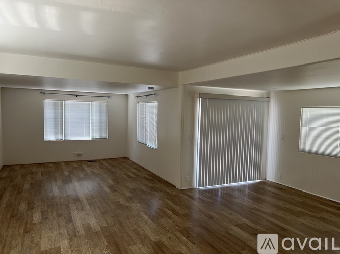 A room with wooden floors and two windows with blinds.