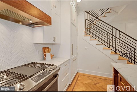 A kitchen with a stove top oven and a staircase with a metal railing.