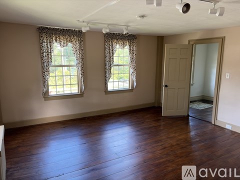 A room with wooden floors and two windows with curtains.