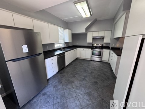 A kitchen with a stainless steel refrigerator and black countertops.
