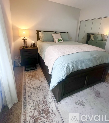 A bedroom with a large bed and a wooden nightstand with a lamp on it.