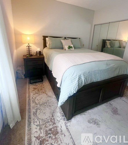 A bedroom with a large bed and a wooden nightstand with a lamp on it.