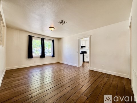 A room with wooden flooring and a window with black curtains.