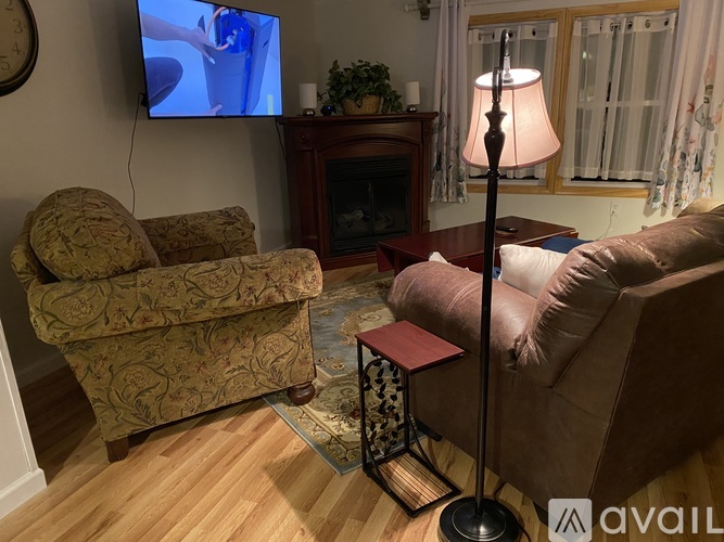 A living room with a sofa, chair, lamp, and a television on the wall.