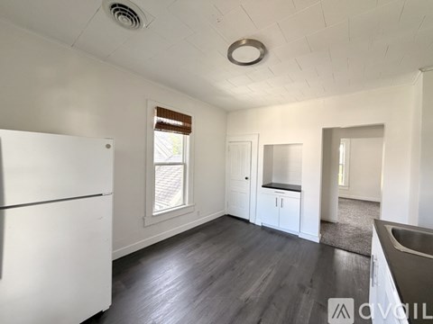 A white refrigerator is in a kitchen with wood floors and white walls.