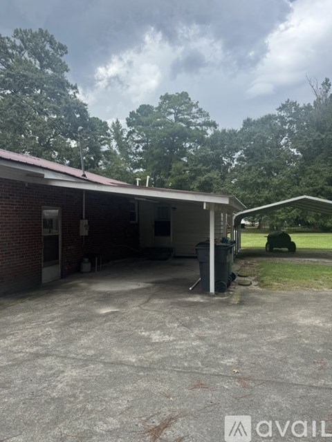 A carport with a brick building and a green lawn in the background.
