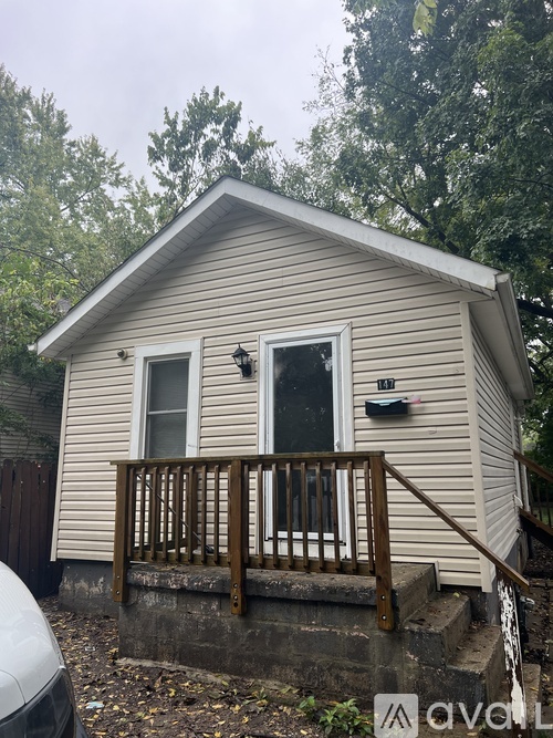 A small house with a porch and a window is surrounded by trees.