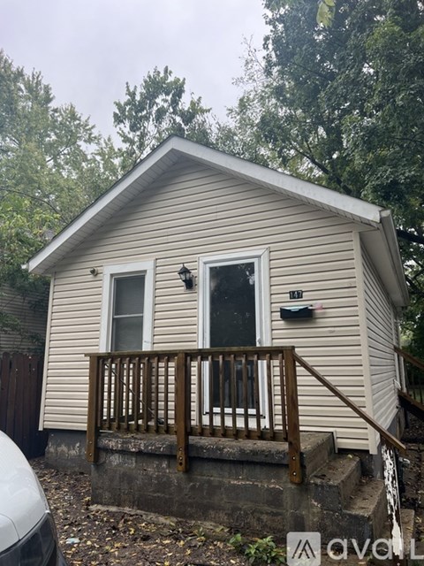 A small house with a porch and a window is surrounded by trees.