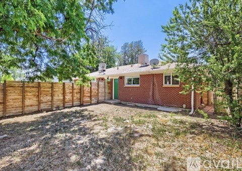 A house with a red brick exterior and a green door is surrounded by a wooden fence and trees.