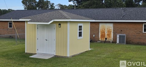A small yellow shed with a white door and a brown roof.