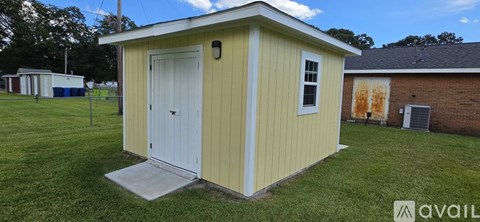 A small yellow shed with a white door stands in a grassy field.