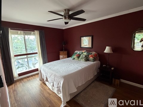 A bedroom with a bed, a ceiling fan, and a window with a view of the outside.