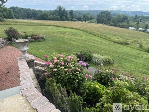 A garden with a stone wall and a statue in the foreground with a grassy field in the background.