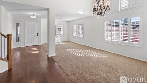 A spacious living room with a chandelier, hardwood floors, and large windows with blinds.